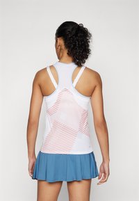 Fehér sportos top geometrikus korall- és világos rózsaszín mintával, kék szoknyával párosítva. Racerback kialakítású és állítható pántokkal rendelkezik.