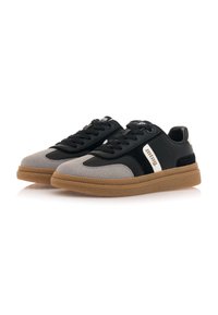Zapatilla negra y gris con suela de goma, diseño con cordones, materiales de ante y cuero, detalle de logo blanco en el lateral y acentos texturizados.