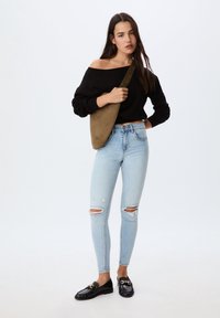 Črna pulover brez naramnic, svetlo modri raztrgani skinny džins, in črne loafer čevlje z zlatimi detajli. Oljčno zeleni torbica preko rame dopolnjuje obleko.