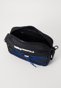 Schwarze Nylon-Crossbody-Tasche mit Reißverschluss, blauen Akzentriemen und silbernem Logodetail auf der Vorderseite. Das Innere verfügt über mehrere Fächer.