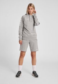 Hoodie cinza com cordão e logótipo, combinado com calções coordenados. Apresenta elementos brancos nas mangas, tecido texturizado e sapatilhas atléticas.