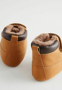 Braune Lederstiefeletten mit braunem Fleece-Futter, runder Form und Zuglaschen hinten. Merkmale sind sichtbare Nähte und eine weiche Textur.