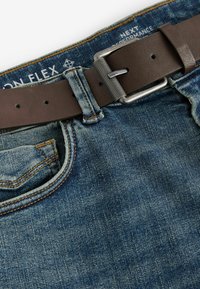 Faded sinine pesu denim teksad, millel on pruun nahast vöö hõbedase metallist pandlaga, oranž õmblus ja esikott.