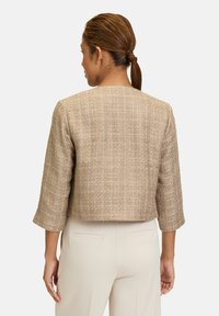 Veste courte en tissu beige texturé avec un motif à carreaux, présentant des manches trois-quarts et un dos épuré.