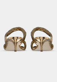 Χρυσά σανδάλια με τακούνια, διασταυρωμένα λουριά με υφή, ανοιχτή πλάτη και λεπτό τακούνι. Το υλικό έχει λαμπερό μεταλλικό φινίρισμα.