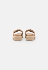 Sandales en caoutchouc tan avec deux sangles torsadées, talon rond et semelle striée. Texture lisse avec un design minimaliste.