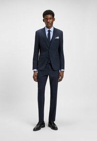 Mörkblå kostym med slim-fit design, slagkrage och tvåknappsstängning. Matchad med en ljusblå randig skjorta och svarta skor.