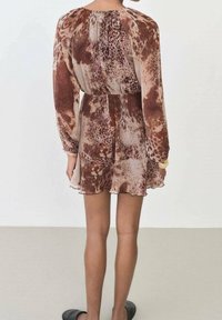 Robe marron et beige avec un imprimé léopard, dotée de manches longues, d'une taille cintrée et d'un ourlet volants. Tissu doux et léger.