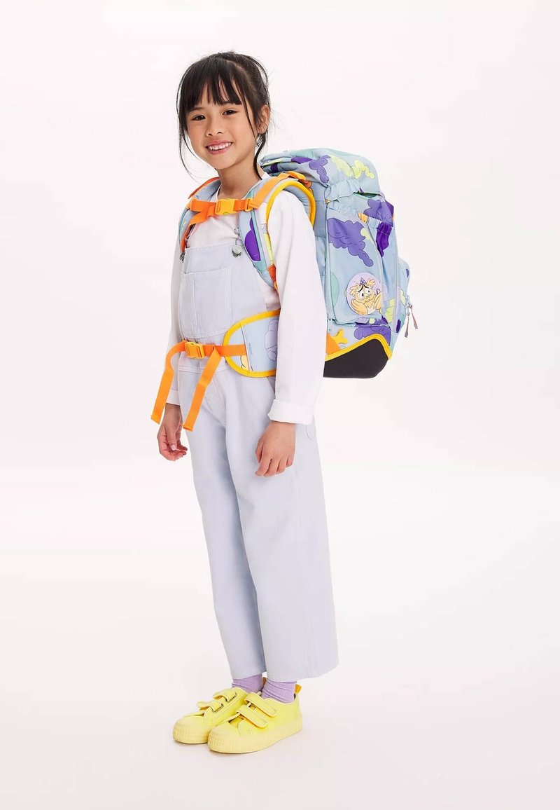 Sac à dos multicolore avec des impressions de nuages et d'animaux, sangles réglables et accessoires orange ; enfant portant une salopette bleu clair et des chaussures jaunes.