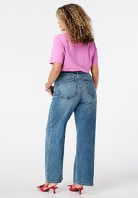 Chemise rose clair à manches courtes associée à un jean droit taille haute bleu et des sandales à talons rouges, avec deux poches arrière.
