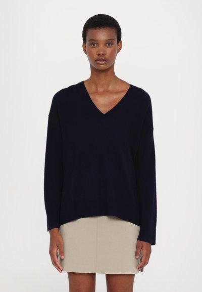 Navy blue v-neck sweater with long sleeves, made from a soft material, paired with a beige fitted skirt. Simple design, no patterns or accents.