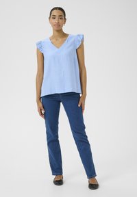 Blouse bleu clair à encolure en V avec des manches courtes froncées, assortie à un jean coupe droite bleu foncé et des ballerines noires. Texture de tissu douce.