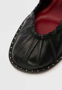 Čierna kožená obuv so záhybovým dizajnom a červenou vnútornou stielkou. Obsahuje strieborné nitmi pozdĺž okraja a zaokrúhlenú špičku. Hladká textúra.