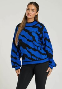 Blå och svart mönstrad stickad tröja med rund halsringning, långa ärmar och ribbade muddar. Mjuk textur med en djärv, abstraherad design.