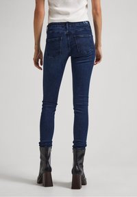 Dark blue skinny jeans with a smooth denim texture. Features two back pockets and a mid-rise waistband, paired with black heeled boots.