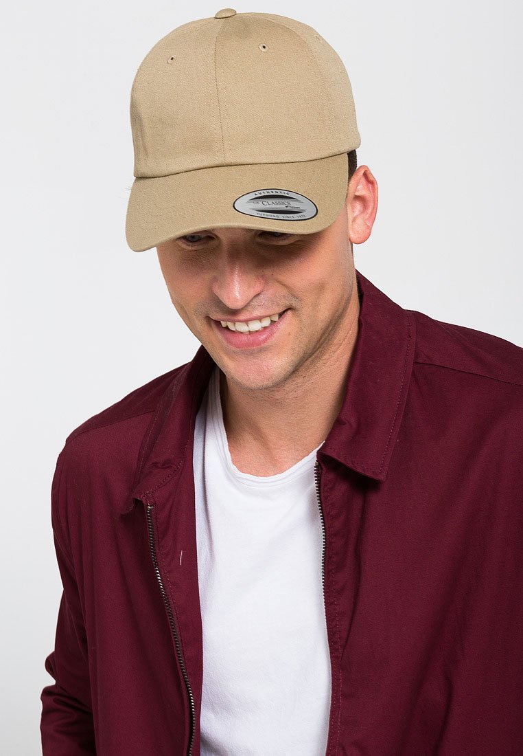 Khaki színű baseball sapka, amit szövetből készítettek, ívelt napellenzővel és hátul állítható pánttal rendelkezik. Egy bordó kabáttal viselik, ami fehér ing felett van.