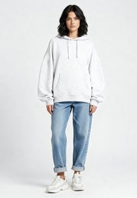 Lichtgrijze hoodie met een losse pasvorm, trekkoorden en een voorzak, gecombineerd met blauw opgerolde spijkerbroek en witte sneakers.