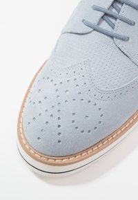 Chaussure oxford en daim bleu clair avec des perforations, surface lisse, embout arrondi et semelle en caoutchouc beige avec des coutures d'accent bleu marine.