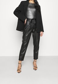 Black blazer over a silver metallic top, with high-waisted black faux leather trousers and black strappy heels. Smooth textures and tailored fit.