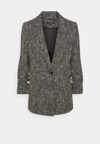 Blazer sur mesure en motif pied-de-poule noir et blanc, avec une fermeture à un seul bouton et des manches légèrement froncées. Tissu doux et texturé.