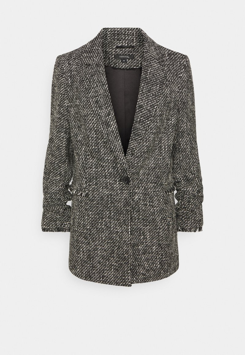 Blazer sur mesure en motif pied-de-poule noir et blanc, avec une fermeture à un seul bouton et des manches légèrement froncées. Tissu doux et texturé.