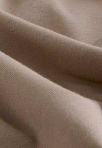 Beżowa dzianina o gładkiej fakturze, z miękkimi, opadającymi fałdami i jednolitym wzorem, eksponująca rozciągliwość i układ materiału.