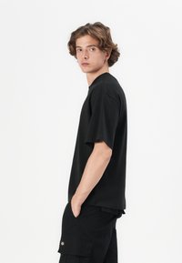 Sort bomulds t-shirt med løs pasform og korte ærmer, med en rund udskæring og minimalistisk design. Enkel og alsidig stil.