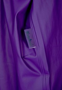 Tecido impermeável roxo com detalhes de fecho éclair e um rótulo da Playshoes visível, exibindo uma textura suave e brilhante.