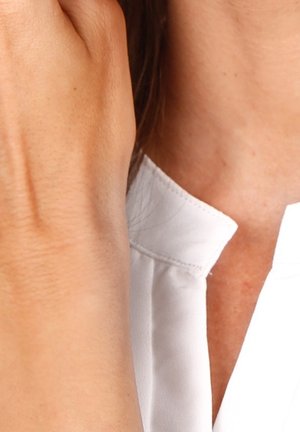 Gros plan d'une personne portant une chemise blanche, la main levée couvrant partiellement son visage et son cou.