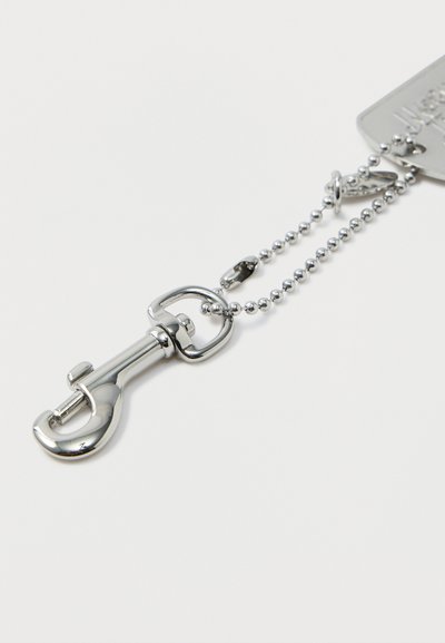 Ασημένιο μεταλλικό κλιπ συνδετήρα προσαρτημένο σε ασημένια αλυσίδα μπίλιας σε λευκό φόντο.