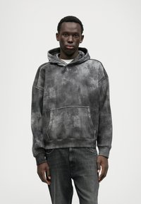 Γκρίζα φαρδιά hoodie με υφή tie-dye, καγκουρό τσέπη και ταιριαστά μανίκια. Συνδυασμένο με σκούρες τζιν πιτζάμες.