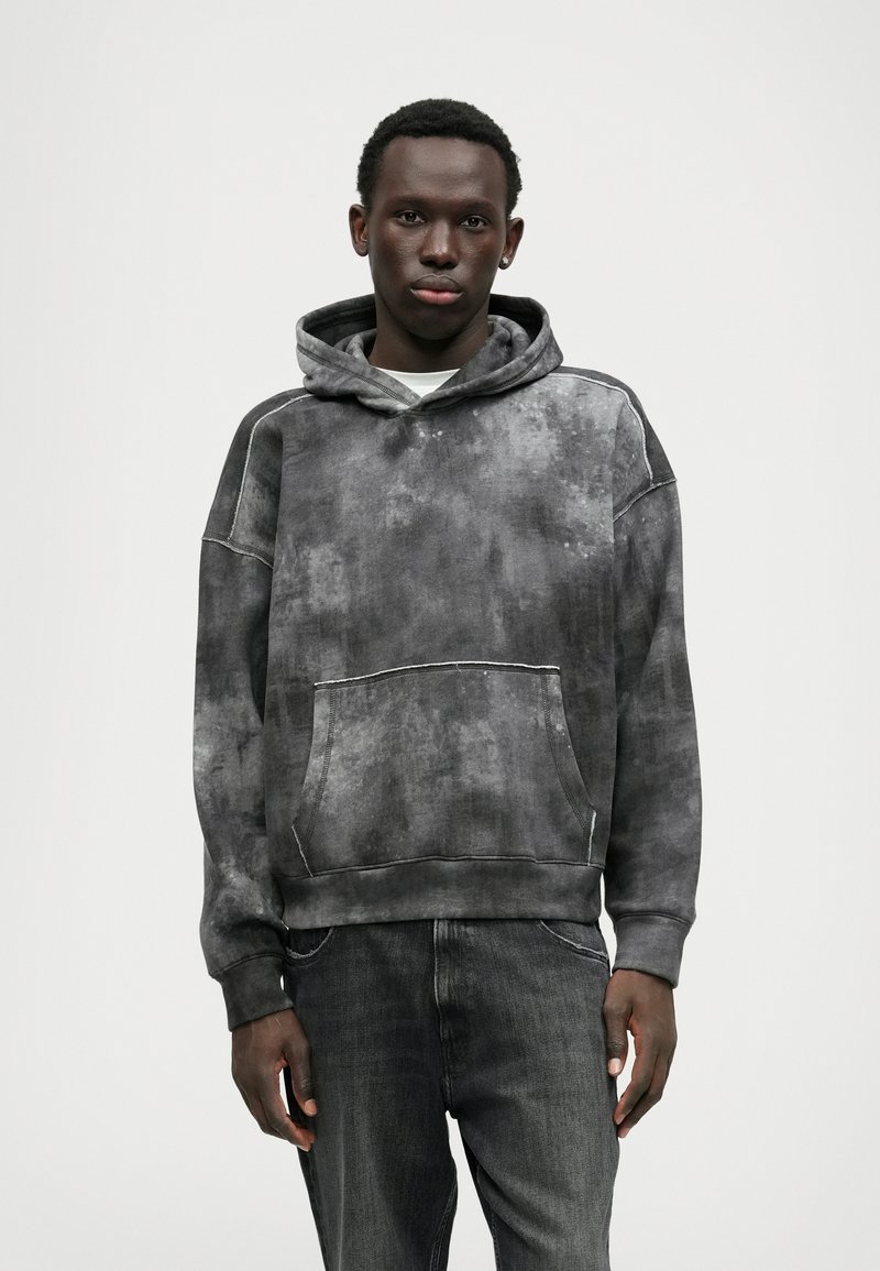 Γκρίζα φαρδιά hoodie με υφή tie-dye, καγκουρό τσέπη και ταιριαστά μανίκια. Συνδυασμένο με σκούρες τζιν πιτζάμες.