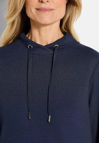 Felpa navy con texture a coste, dotata di un collo incrociato e di cordini regolabili con estremità metalliche. Design semplice e funzionale.