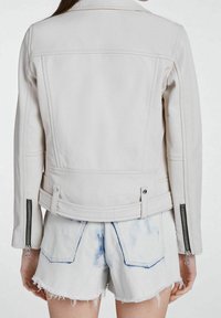 Jasna sztuczna skórzana kurtka o dopasowanym kroju, z zamykanymi na zamek mankietami i strukturalnym tyłem, zestawiona z postrzępionymi szortami dżinsowymi.