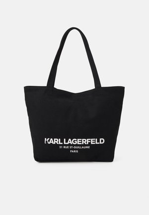 Czarna torba typu tote z dwoma uchwytami na ramię i białym napisem „KARL LAGERFELD 21 RUE ST-GUILLAUME PARIS” na środku z przodu.