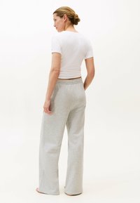 Grijze sweatpants van zacht materiaal, met een relaxte pasvorm en een elastische tailleband. Gecombineerd met een fitted wit T-shirt met korte mouwen.