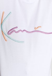 Biała bawełniana koszulka z kolorowym haftowanym tekstem w pastelowych odcieniach różu, niebieskiego i pomarańczowego, z płynnymi, artystycznymi liniami.