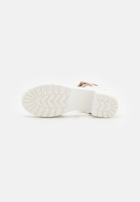 White rubber shoe sole with a textured, zigzag pattern. Includes a smooth midsole and a small section of tan material at the heel.