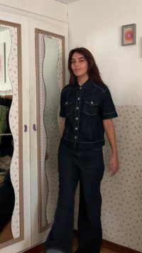 Svart denimskjorta med korta ärmar, framfickor och vit sömnad, kombinerad med svarta utsvängda byxor. Spegelvänt garderob i bakgrunden.