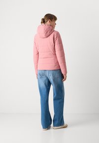 Gevoerde roze jas met een capuchon, voorzien van een horizontaal gestikt ontwerp en elastische manchetten, gecombineerd met blauwe wijde jeans en beige sneakers.