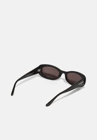 Sunglasses with a sleek black plastic frame, curved lenses, and narrow temples. Lenses have a dark tint, featuring the brand "vogue" on the side.