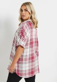 Camisa de cuadros de manga corta en rosa, rojo y blanco; presenta un ajuste relajado, dobladillo curvado y un pliegue en la parte trasera para mayor movimiento.