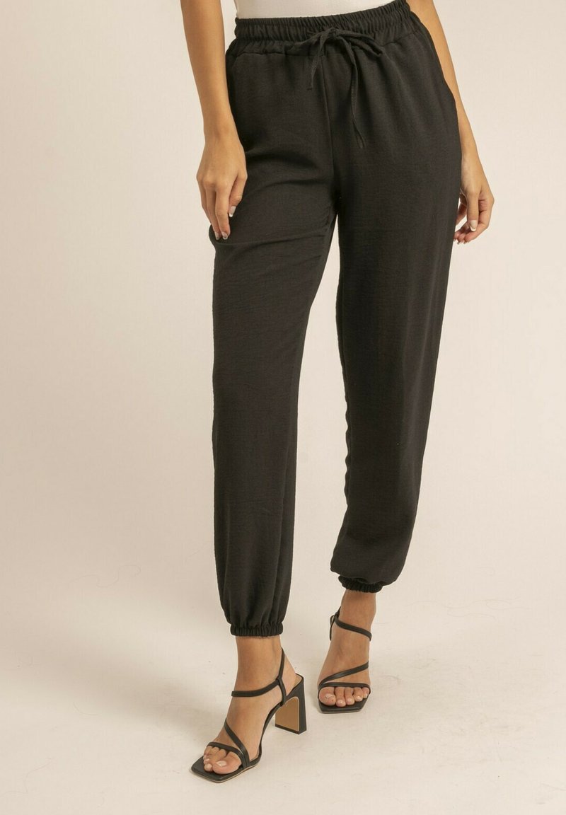 Pantalons noirs, légers, avec une taille élastique et des chevilles resserrées. Associés à des sandales à talons carrés avec des lanières.