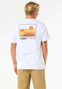 White cotton t-shirt with a retro sunset graphic in orange and yellow on the back, featuring the "Rip Curl" logo in black.