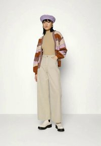 Cardigan riscado em castanho, rosa e lavanda, blusa bege, calças largas beges e um boina lavanda. Sapatos de sola grossa pretos.