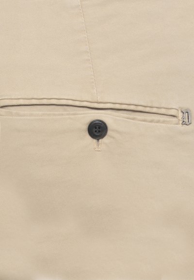 Pantaloni in tessuto beige con una tasca posteriore con bottone e un piccolo emblema decorativo in metallo sul bordo della tasca.