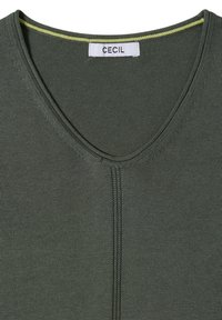 T-shirt en maille vert foncé avec un col en V, une couture verticale centrale et une étiquette blanche avec le nom de la marque Cecil à l'intérieur du col.