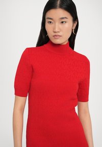 Bluza roșie tricotată cu mâneci scurte și guler înalt. Prezintă un model texturat și o siluetă mulată. Material neted.