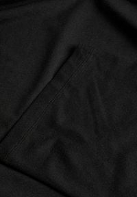 Κοντινή λήψη μαύρου υφάσματος που δείχνει μια ραμμένη ορθογώνια τσέπη με ορατά γαζιά και ελαφρά ζάρωμα στο υλικό.