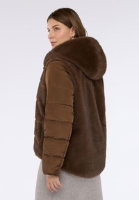 Gilet imbottito marrone con cappuccio in pelliccia sintetica, caratterizzato da un fronte dalla texture liscia e un retro morbido e soffice. Progettato con ampi fori per le braccia e una vestibilità comoda.